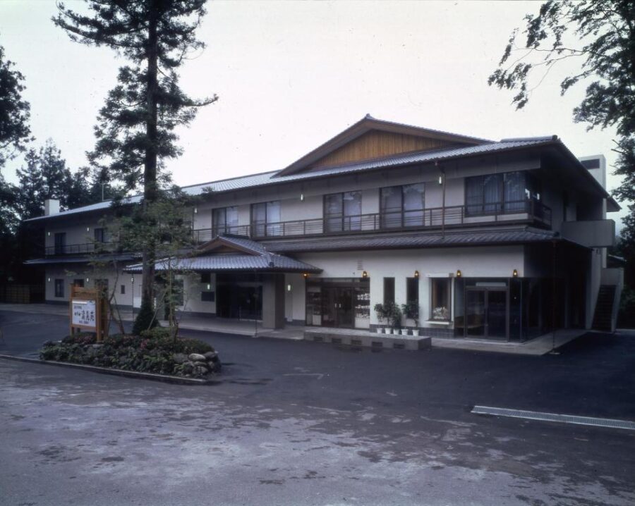 Traditional Japanese inn hotel in forest setting with parking lot and wet pavement after rain.