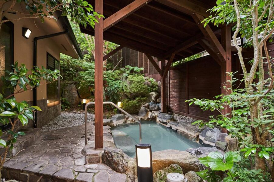 Tranquil Japanese onsen in lush garden with rustic wooden beams and stone path.