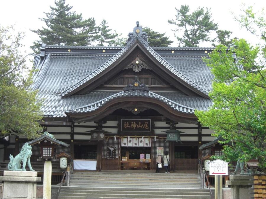 Traditional Japanese Shinto shrine in Kanazawa with tiled roof, stone steps, komainu statues and greenery.