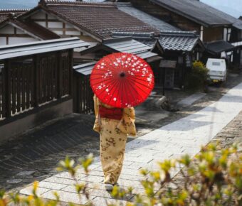 Traditional Japanese street scene with person in kimono, red parasol, and wooden buildings.
