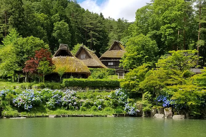Traditional Japanese thatched roof village by forested hillside and pond with hydrangea flowers.