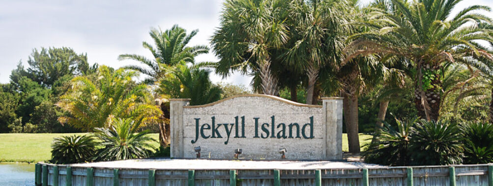 Entrance sign to Jekyll Island framed by palm trees on a warm summer day.