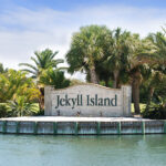 Entrance sign to Jekyll Island framed by palm trees on a warm summer day.