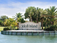 Entrance sign to Jekyll Island framed by palm trees on a warm summer day.