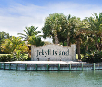 Entrance sign to Jekyll Island framed by palm trees on a warm summer day.