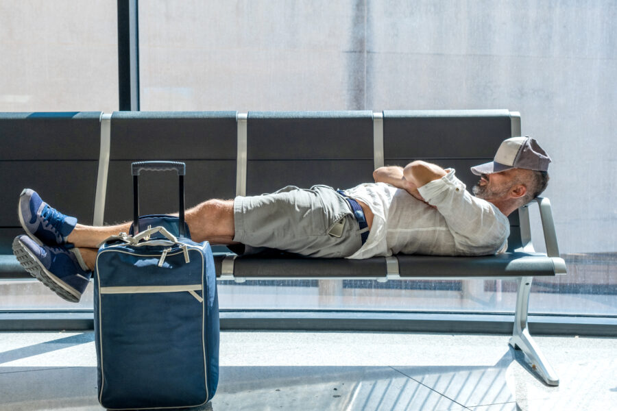 Man rests on armchairs in an airport, struggling with jet lag as he sleeps amidst the bustling terminal