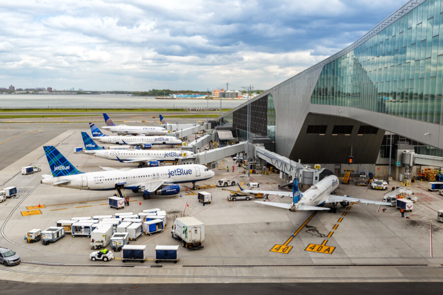 JetBlue airplanes parked at Terminal B, a large building with numerous windows at LaGuardia Airport, New York.