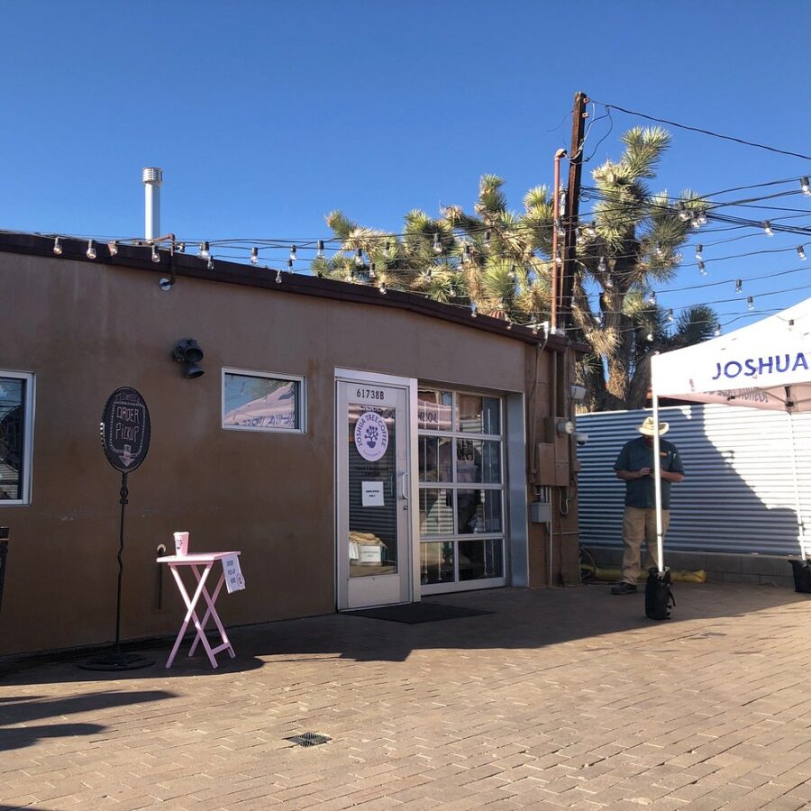 The Joshua Tree Coffee Company building with a pink umbrella on the sidewalk, inviting customers to sit outside.