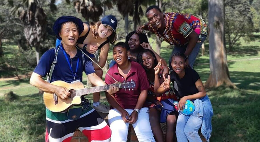 Joyful diverse group gathering outdoors with guitar, enjoying music, nature, and camaraderie.