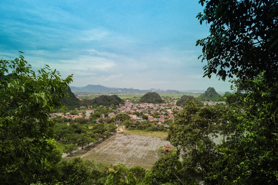Scenic karst valley town with rice fields, green hills, and rural landscape under blue sky.