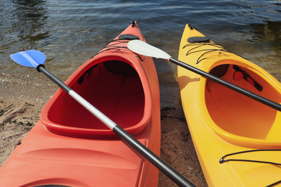 Kayaks with paddles resting on the beach beside a river, ready for an adventure in the water