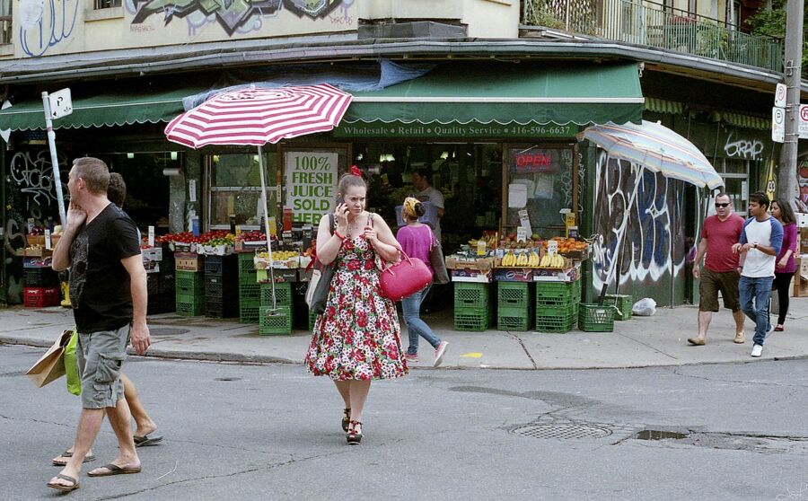 Kensington Market, Canada, a woman strolls down the street, carrying an umbrella for protection from the elements.
