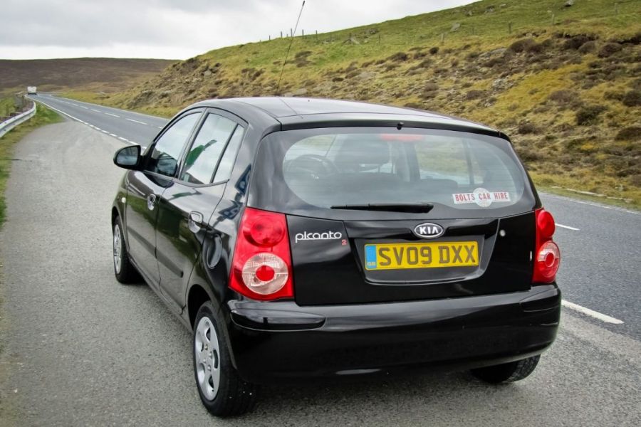 Kia Picanto rental car on scenic rural road with dramatic hills.