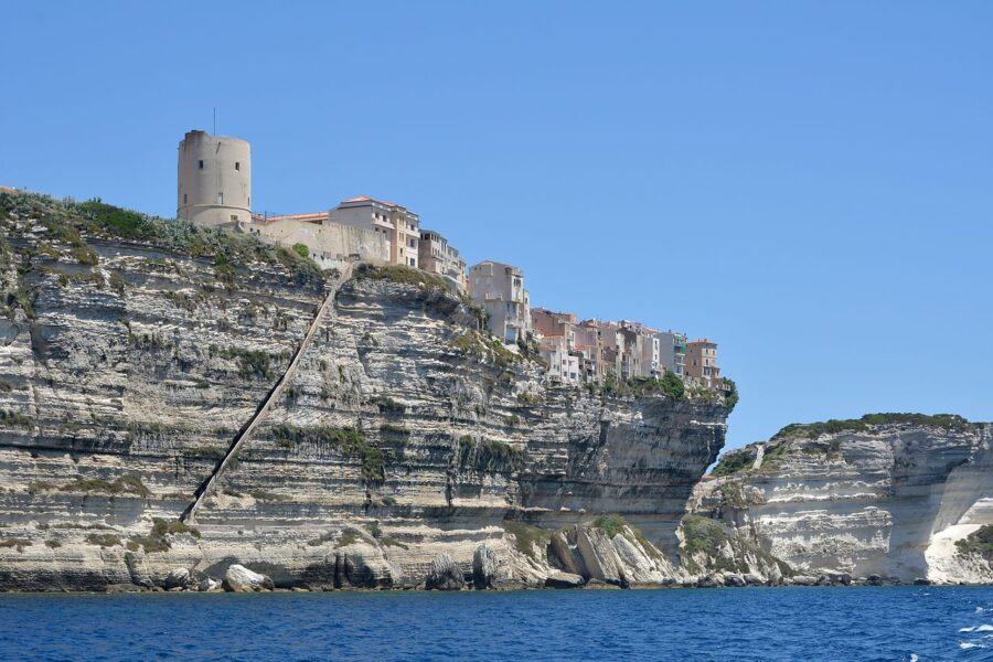 Scenic view of the King of Aragon’s Staircase, featuring a building atop a steep cliff in Corsica, France.