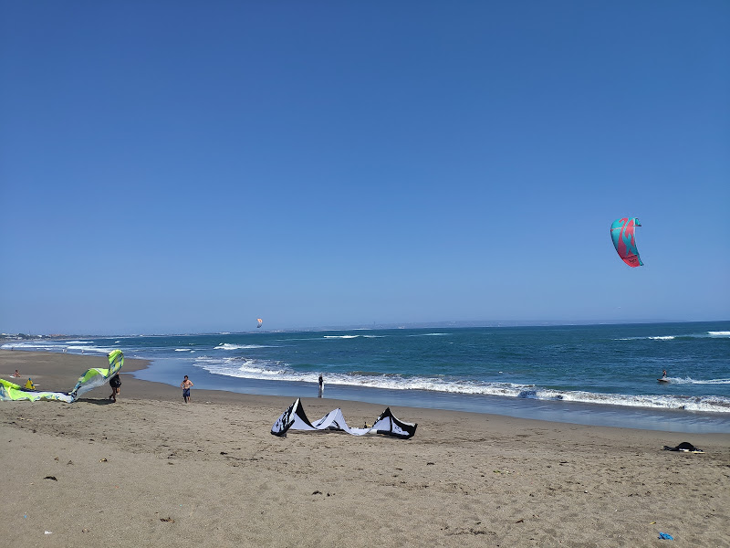 Kitesurfers on wide sandy beach with azure sea, clear blue sky and breaking waves.