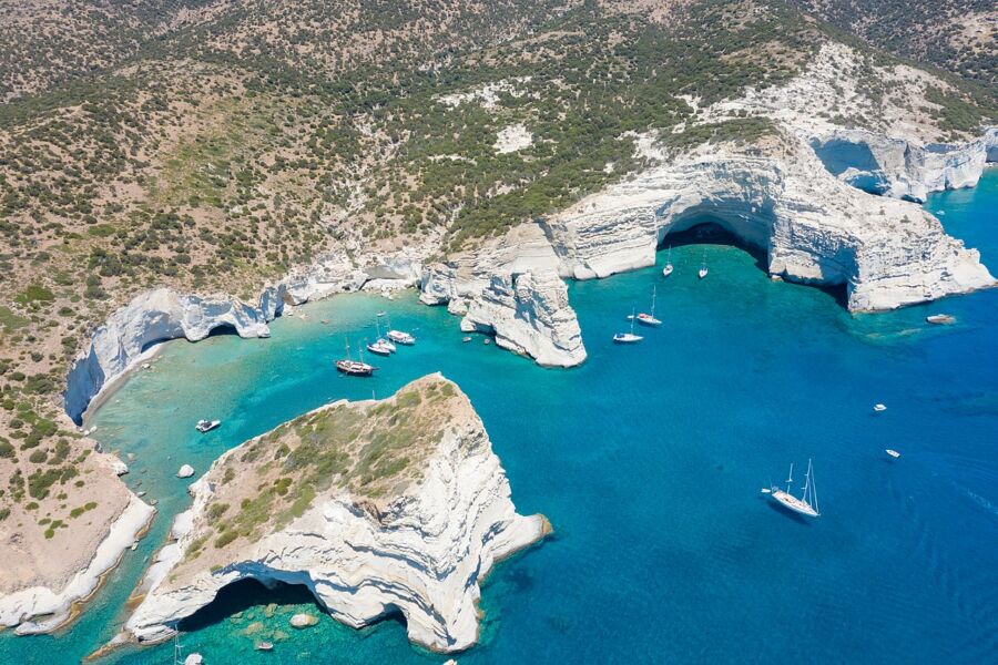 Aerial view of Kleftiko Bay, Milos Island, Greece, showcasing white cliffs and boats in the turquoise water.
