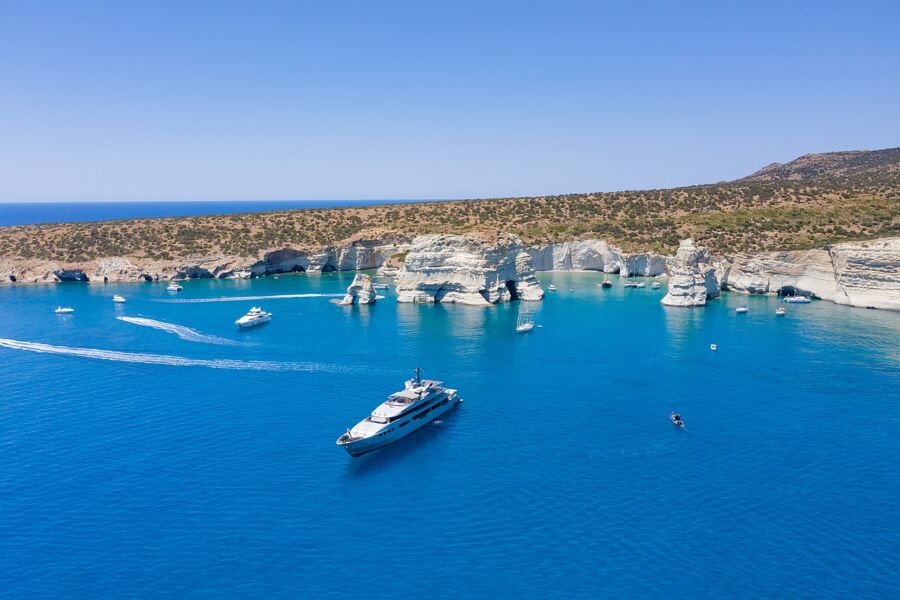 Boat rests in the clear blue water by the cliffs of Kleftiko, Milos, highlighting the area's natural beauty.