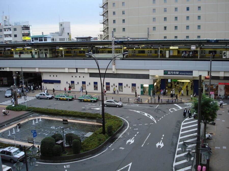 Bustling Kōenji Station in Tokyo at twilight with trains, traffic, pedestrians, and urban scenery.