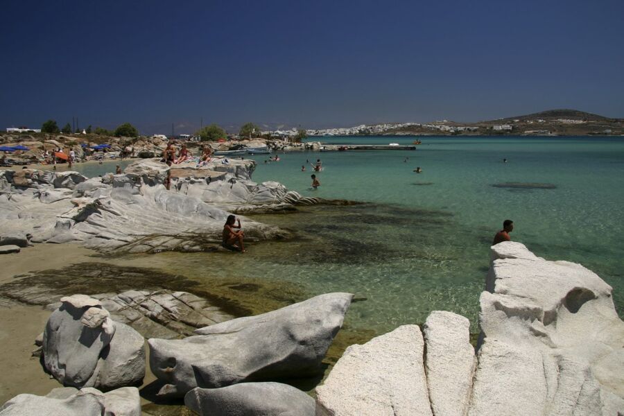 Kolympithres Beach with rocky shores and people enjoying swimming in the clear blue water under a sunny sky.