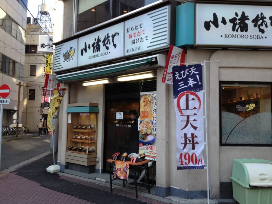 Komoro Soba corner noodle shop with plastic food displays and price banners.
