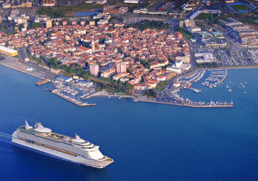 Large cruise ship sailing in the water off the coast of Koper, Slovenia, surrounded by calm waves and distant hills.