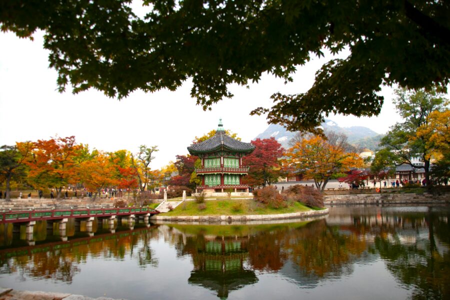 Traditional Korean pavilion in autumn landscape with vibrant foliage and a serene lake reflection.