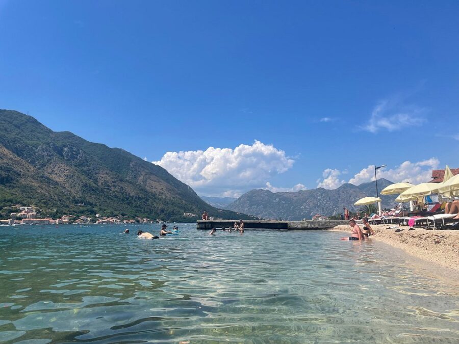 People swimming in the clear waters of Kotor Beach, enjoying a sunny day by the shore.