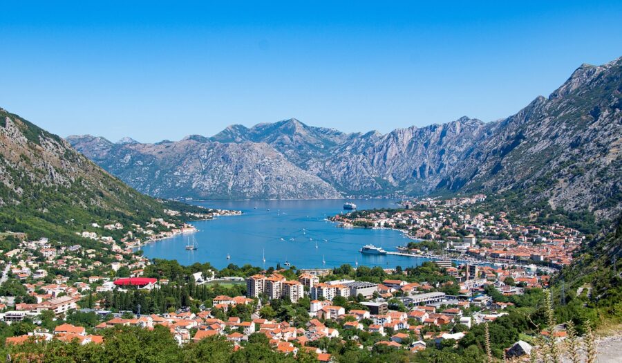 Coastal landscape of Bay of Kotor with mountains, terracotta-roofed town, and vibrant blue waters.