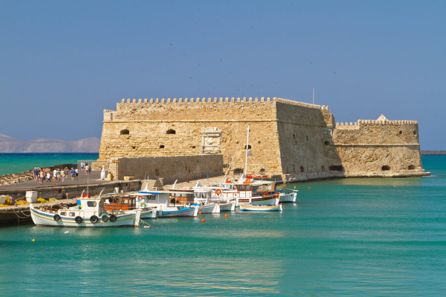 Koules Fortress by turquoise sea, with small boats docked nearby in Heraklion, Crete, Greece