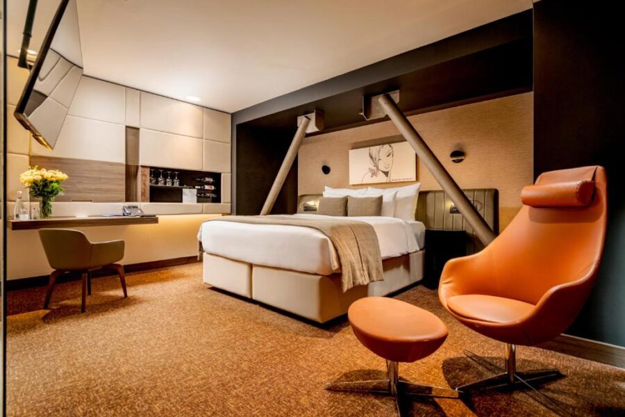 Hotel room at Kronwell Brasov with a bed, chair, and desk, featuring modern decor and warm lighting.