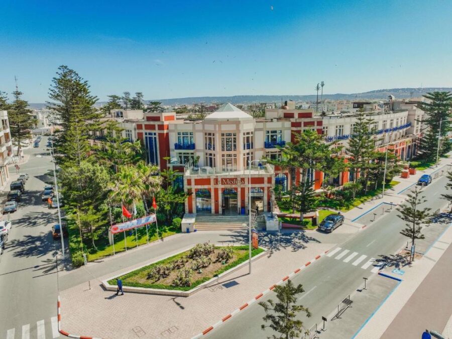 Modern government building in sunny Essaouira cityscape with wide streets, trees and mountains.
