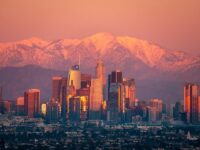Los Angeles skyline at sunset with snowy mountain backdrop, blending urban and natural beauty.