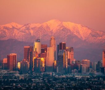 Los Angeles skyline at sunset with snowy mountain backdrop, blending urban and natural beauty.
