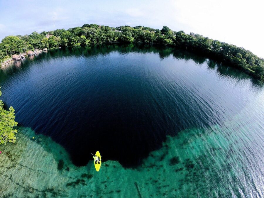 Lone kayaker navigates the tranquil lake of Los Rápidos de Bacalar, Mexico, with vibrant blue waters in the background.