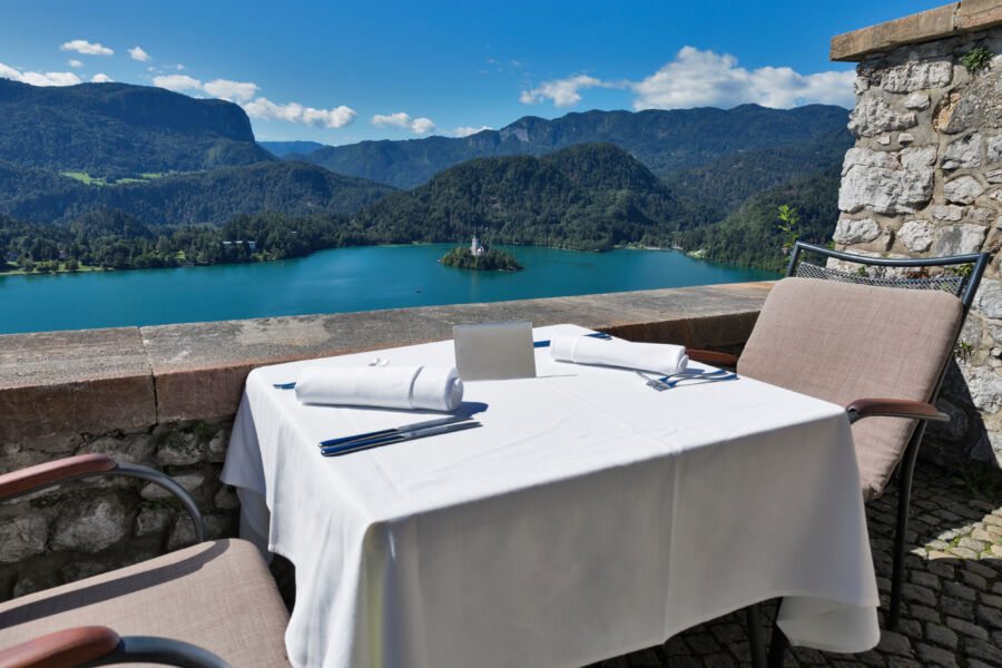Restaurant table set with an empty plate, overlooking Lake Bled, the island, and the Alps in the background