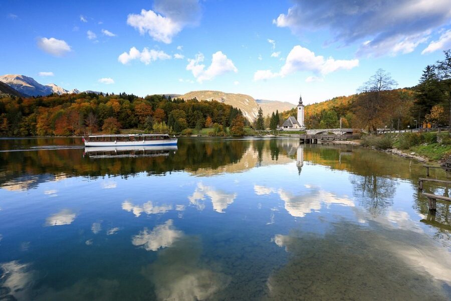 Boat rests at the dock on Lake Bohinj, with a picturesque church standing nearby against a tranquil backdrop.
