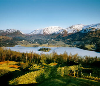 Aerial view of Grasmere village in winter, featuring a frozen lake and snow-covered mountains in Lake District National Park.