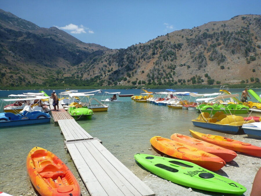 Scenic lakeside with colorful kayaks and paddle boats, surrounded by mountains and clear water.