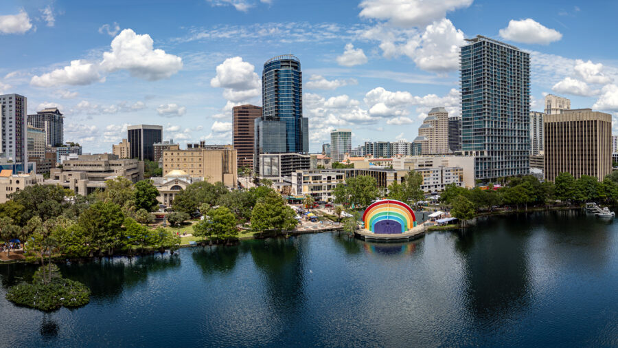 Panoramic view of downtown Orlando, Florida, showcasing skyline above Lake Eola with lush greenery and blue skies.