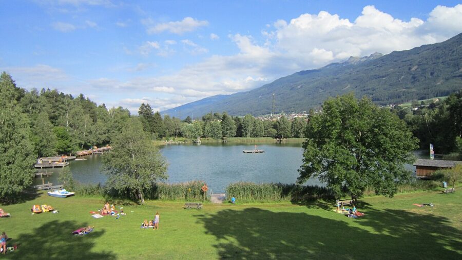 People relaxing on the grass by Lake Lans in Innsbruck, Austria, enjoying a sunny day by the water.