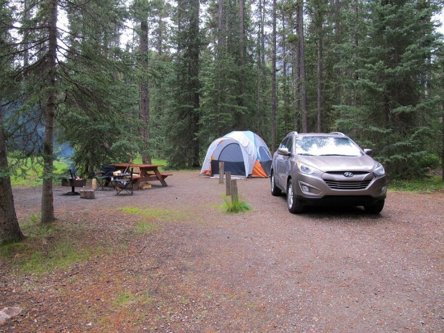 Car is parked by a tent at Lake Louise Campground, with a backdrop of trees and the Canadian wilderness.