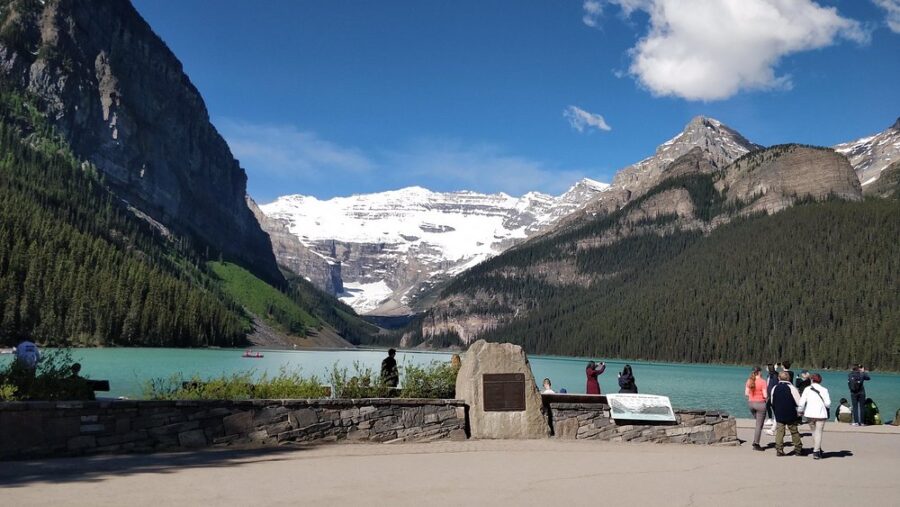 People gather around Lake Louise, with a stunning mountain range in the background, enjoying the scenic beauty of Banff.
