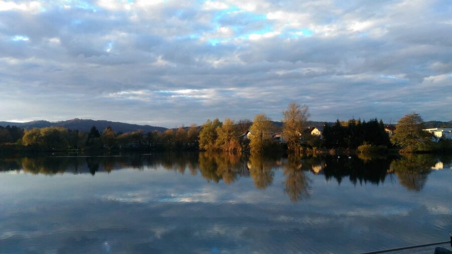 Koseze Pond autumn lake with calm, mirror-like reflections and shoreline trees.