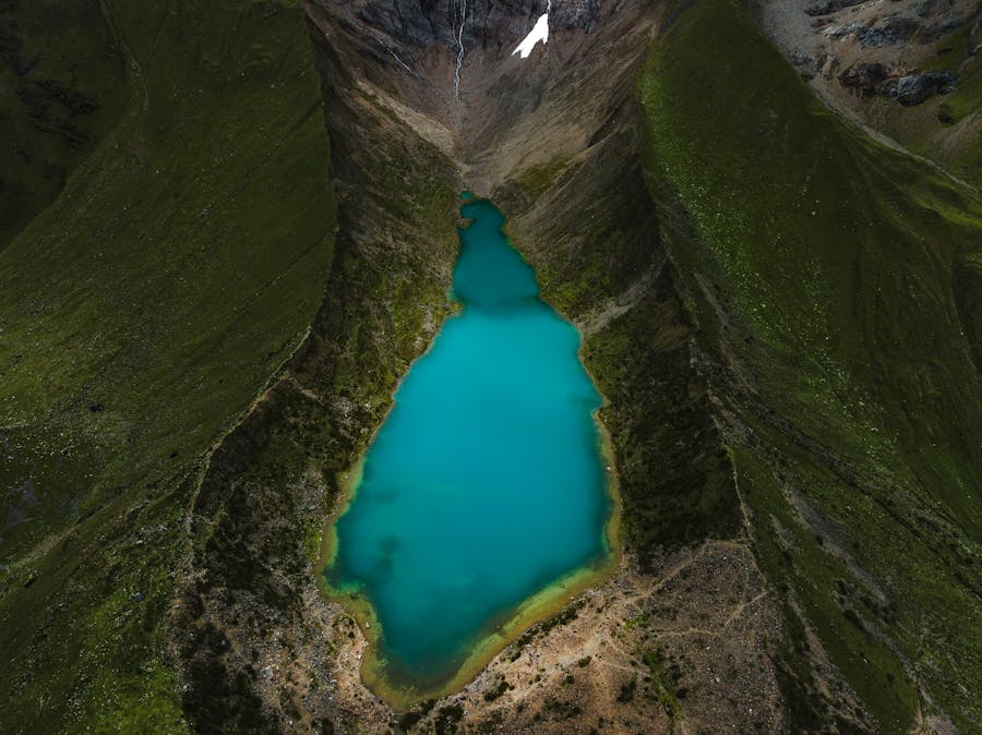 Turquoise alpine lake in lush valley with snow-capped mountains and vibrant greenery.