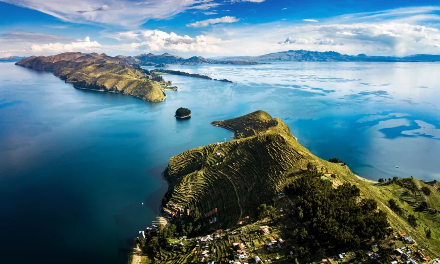 Aerial view of Lake Titicaca with terraced hills and mountain backdrop.