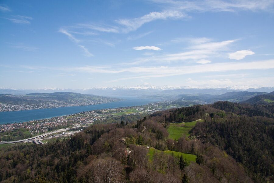 A serene landscape with rolling hills, a tranquil lake, and distant snow-capped mountains.