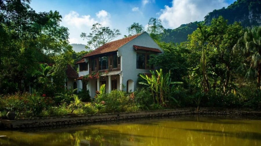 Lakefront garden villa resort in Tam Coc with tropical plants, pond, and mountain views.