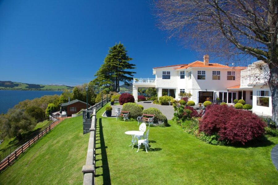 Luxury lakefront villa garden with lawn, patio seating, manicured shrubs, and panoramic water views.