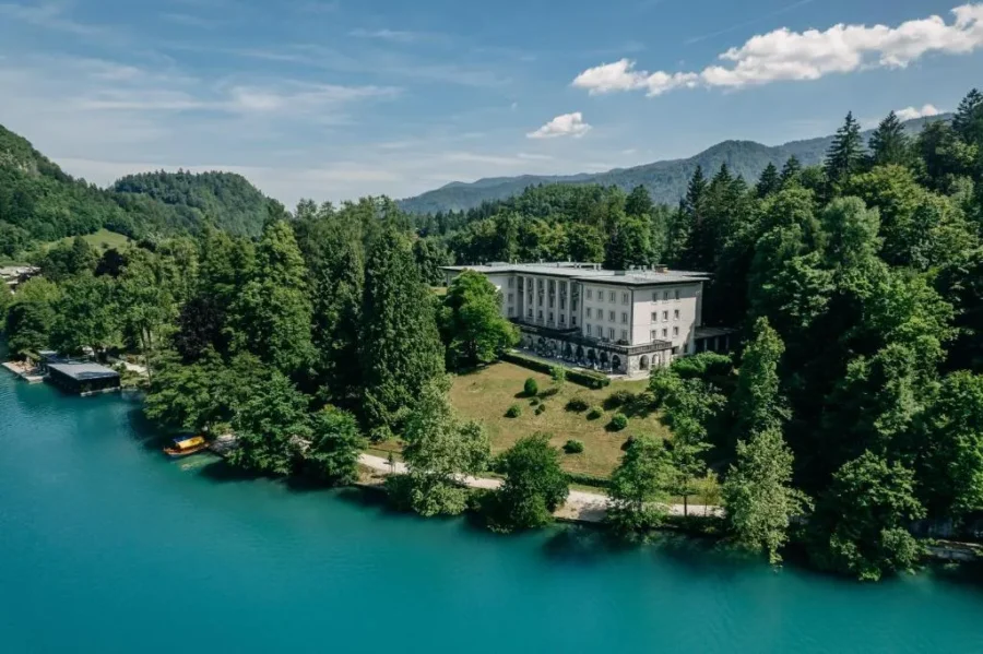 Lake Bled lakeside hotel by turquoise lake and forested mountains.