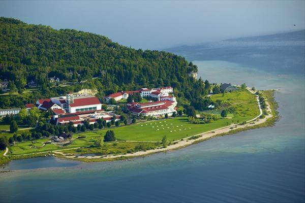 Aerial view of Mission Point Resort on a forested lakeside peninsula with beach and lawns.
